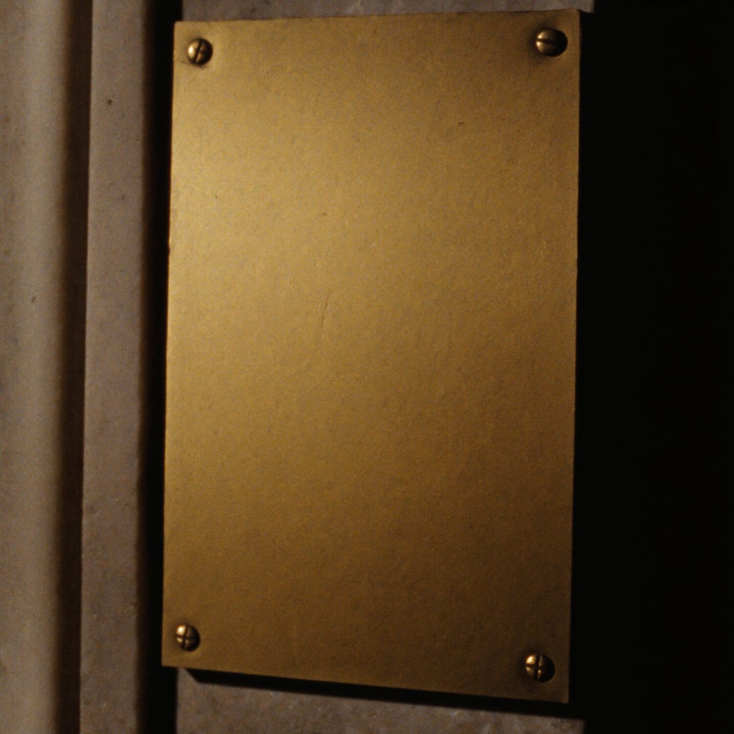 Una placa de bronce sin grabar, atornillada al muro junto a la entrada